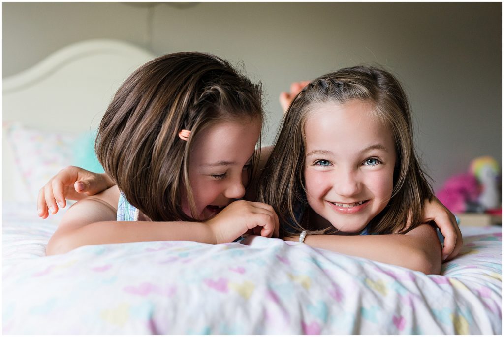 Sisters giggling on bed in an at-home family session in Edina, MN