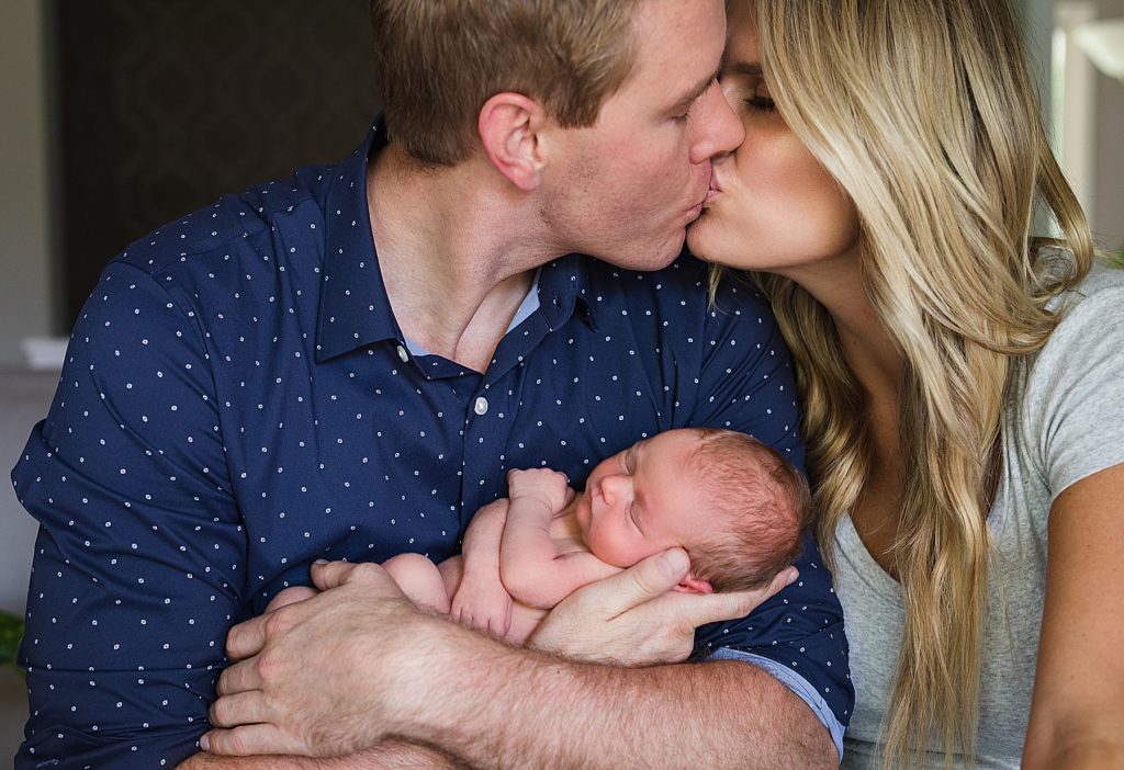 Parents kissing while holding newborn baby