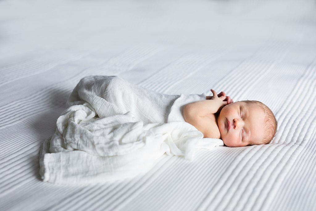 Newborn baby in a swaddle on white bedding