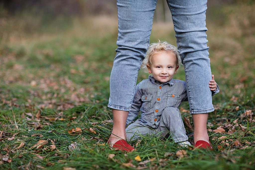 Child sitting on ground between adult legs in photographing kid personalities. 