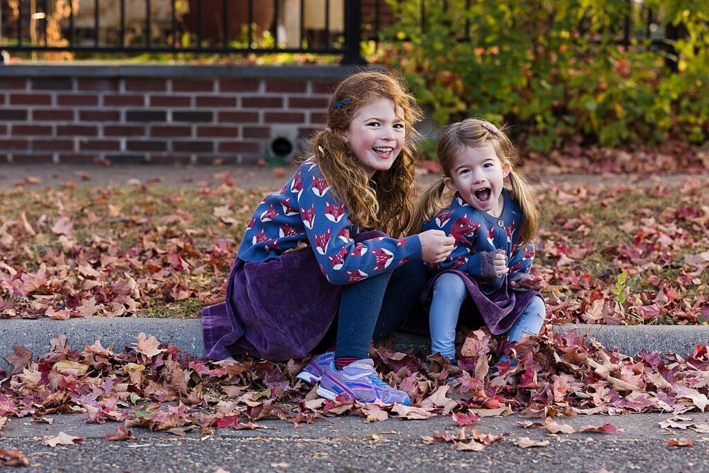 Sisters smiling in fall with red and oranges leaves in St. Paul, MN