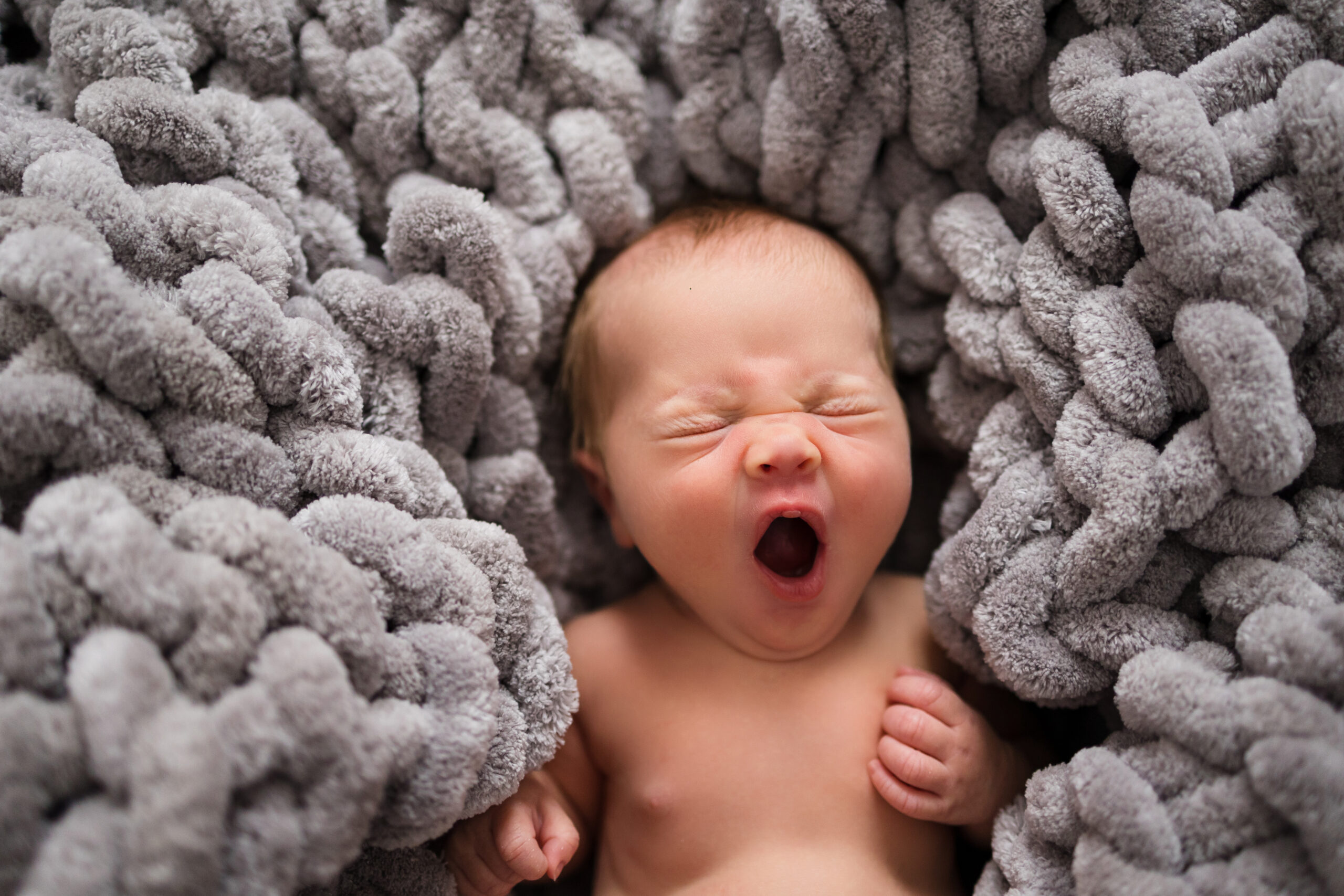 newborn baby laying on a grey large knit blanket