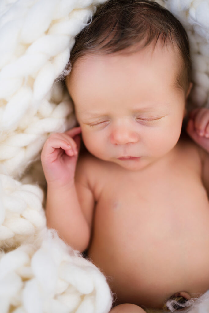 Newborn baby sleeping peacefully on soft white knit blanket, tiny hand resting gently near face.