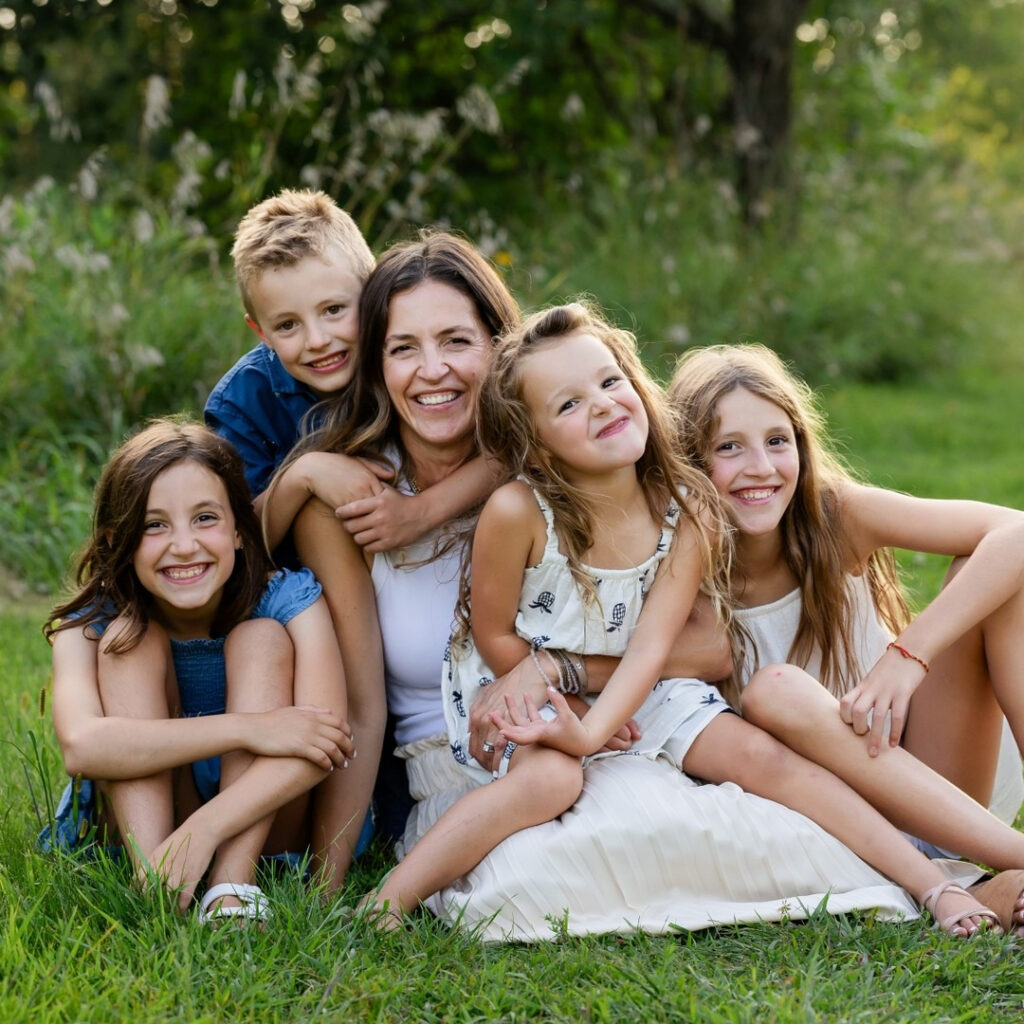 Mom surrounded by her smiling kids during outdoor mom and me photoshoot on a sunny evening.