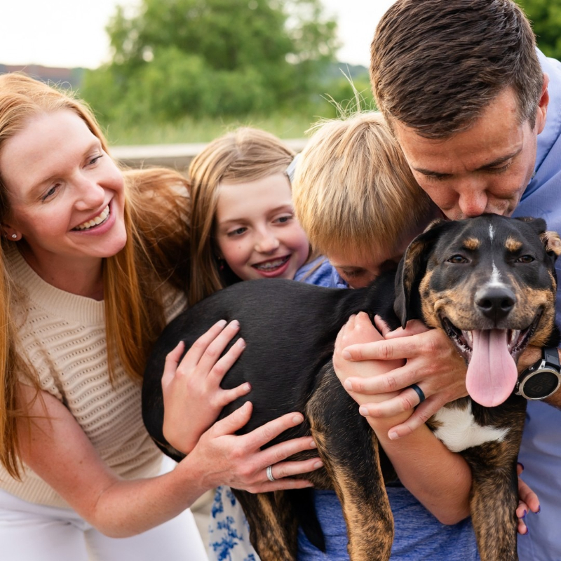 Family smiling and cuddling their happy dog during an outdoor moment filled with laughter and love.