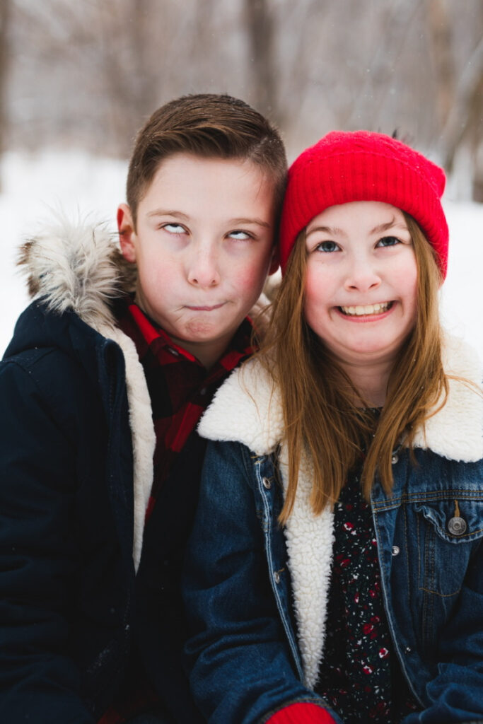 Two kids making silly faces during a lighthearted winter family photoshoot experience outdoors.