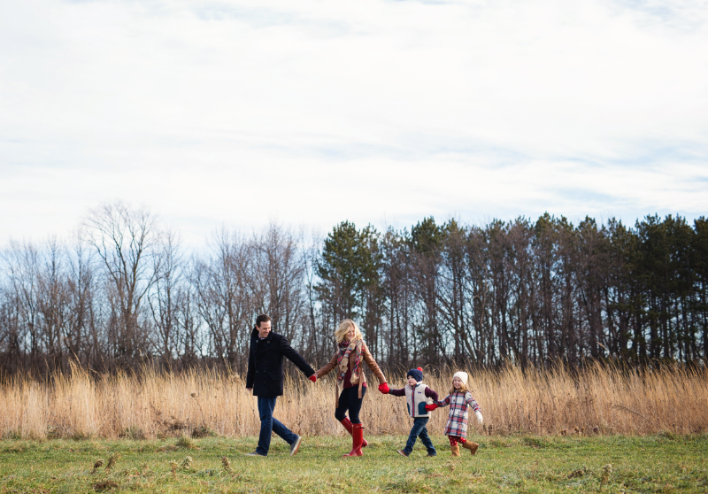 Family holding hands and walking through a field during a joyful outdoor family photoshoot experience.