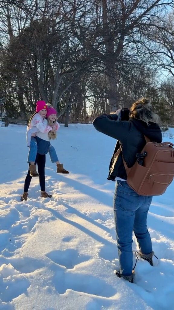 Photographer capturing two smiling girls in winter clothes during a playful outdoor family photoshoot experience.