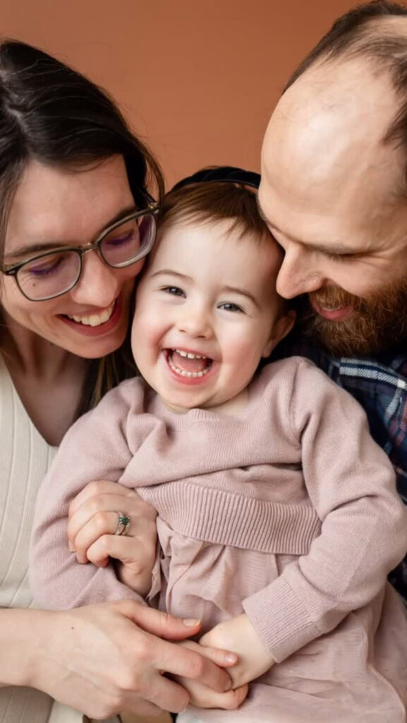 Smiling parents cuddle their toddler during a joyful in-home session, showcasing indoor photo locations in Minneapolis.