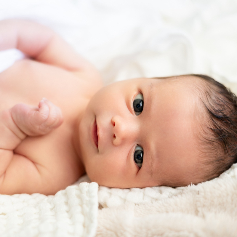 Newborn baby lying on soft blankets, wide-eyed and alert, a sweet moment for postpartum care kit.