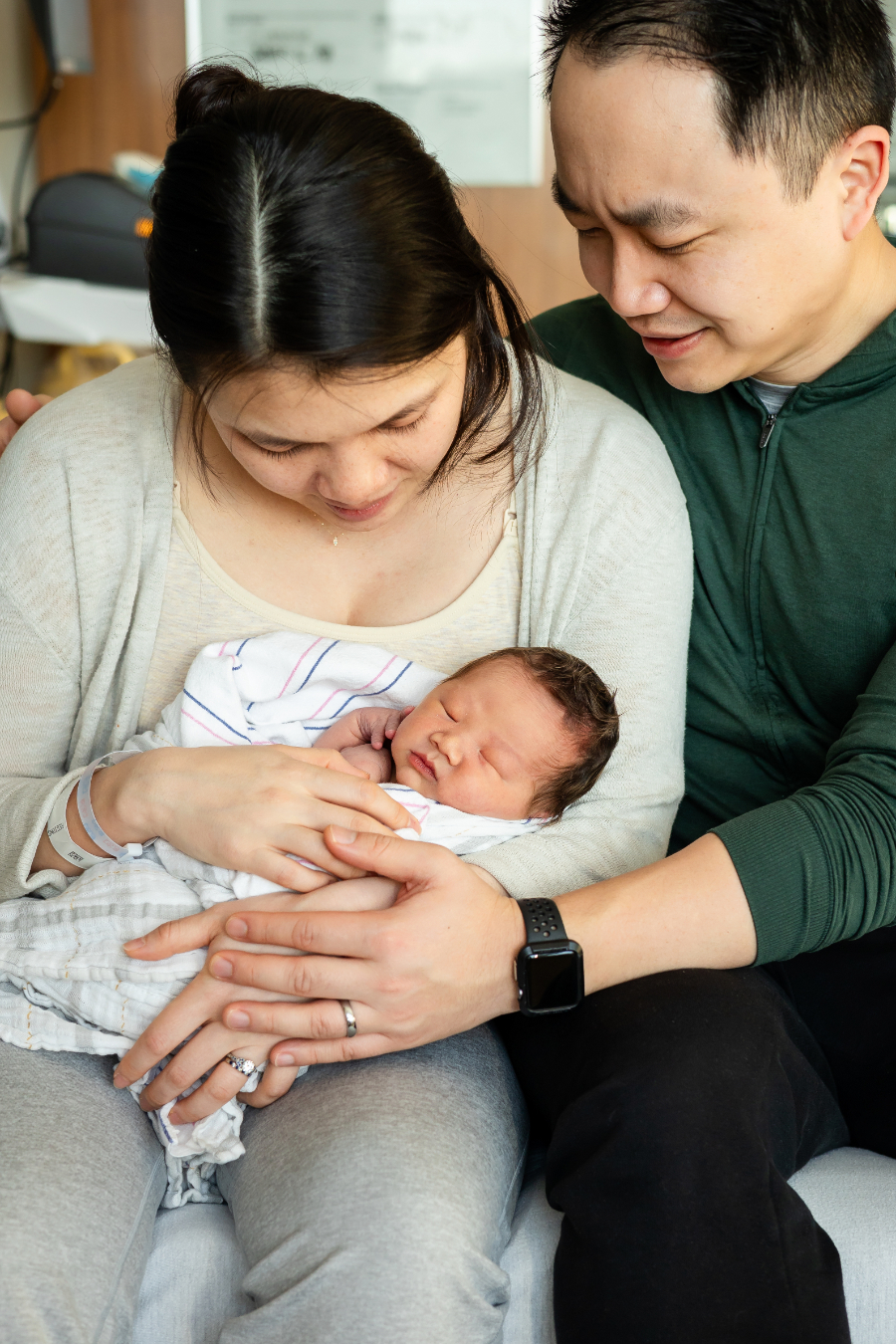 New parents gazing down at their sleeping newborn in a hospital room during a Fresh 48 session with Minneapolis newborn photographer Megan Norman.
