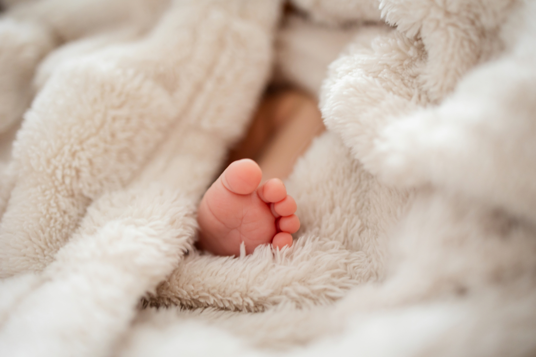 Newborn baby feet tucked into a soft cream blanket, a quiet moment of rest captured during overnight postpartum support.