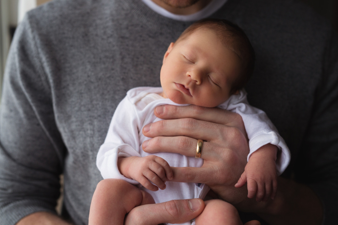 A parent cradling a sleeping newborn against their chest, the kind of peaceful moment a night nurse helps make possible for the whole family.