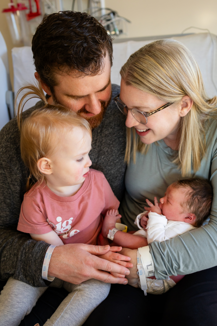 Mom, dad, and toddler big sister snuggle their newborn during a hospital Fresh 48 session in Minnesota.