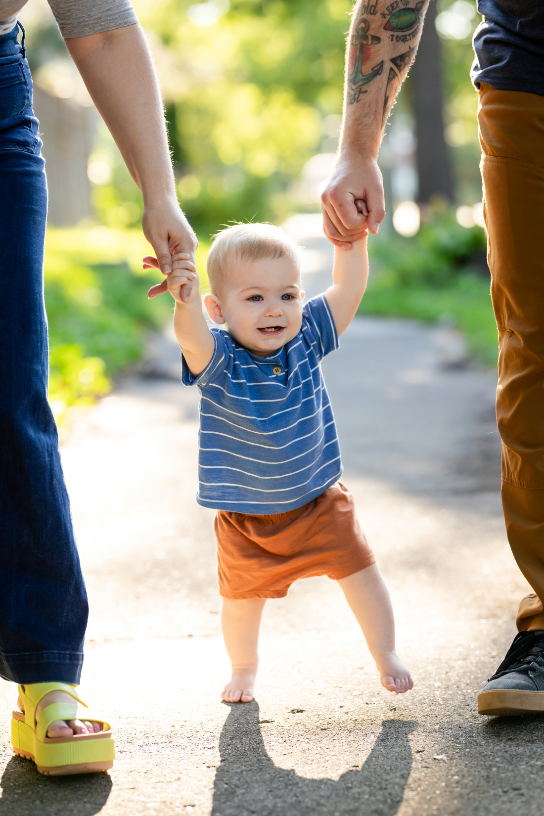 Toddler taking first steps while holding both parents' hands, highlighting storytelling in family photography and meaningful family milestones.