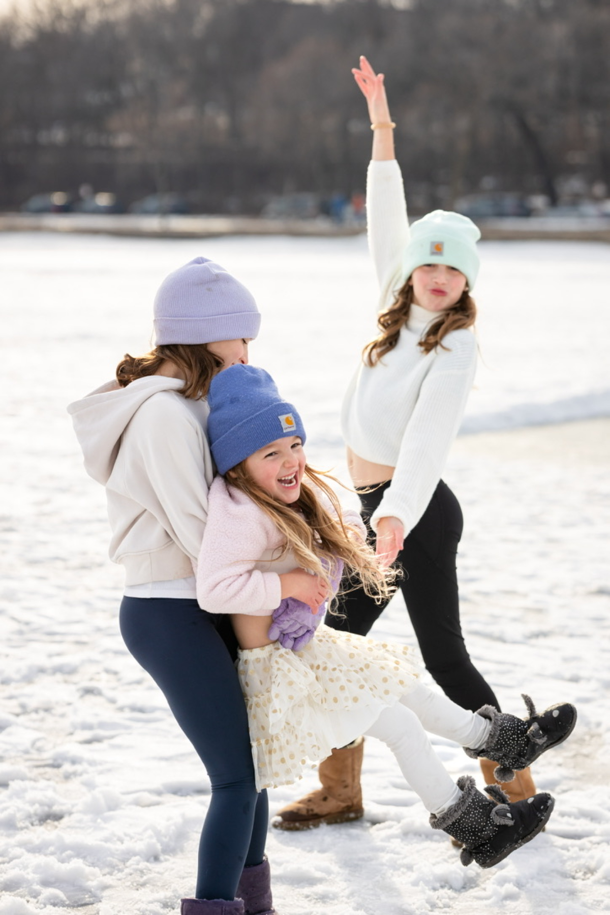 Three sisters spin and play in the snow near a frozen Minneapolis lake during winter minis, caught mid-movement instead of posed.