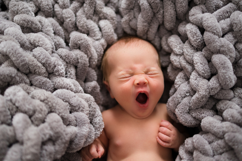 A sleepy newborn yawns while snuggled into a soft gray blanket, a sweet reminder that Birth Plans are only the beginning of the real, beautifully unpredictable newborn days.