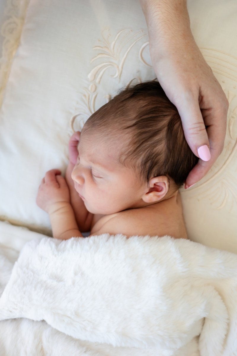Sleeping newborn tucked under a soft white blanket as mom rests her hand on his head, a quiet moment that shows why postpartum nutrition matters for Minnesota moms.