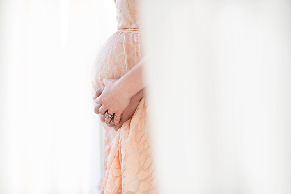 Expecting mom cradles her baby bump in a soft peach dress during a Twin Cities maternity photography session, capturing the anticipation of welcoming her baby.